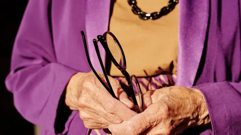 Mãos de uma senhora idosa segurando um par de óculos, com as articulações afetadas pela artrose nos dedos da mão