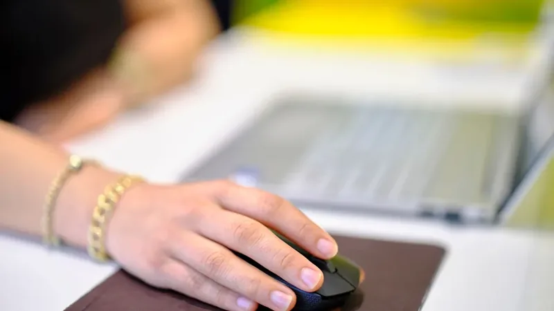Mão usando um mouse ao lado do notebook, postura do punho que ajuda a aliviar a dor do túnel do carpo
