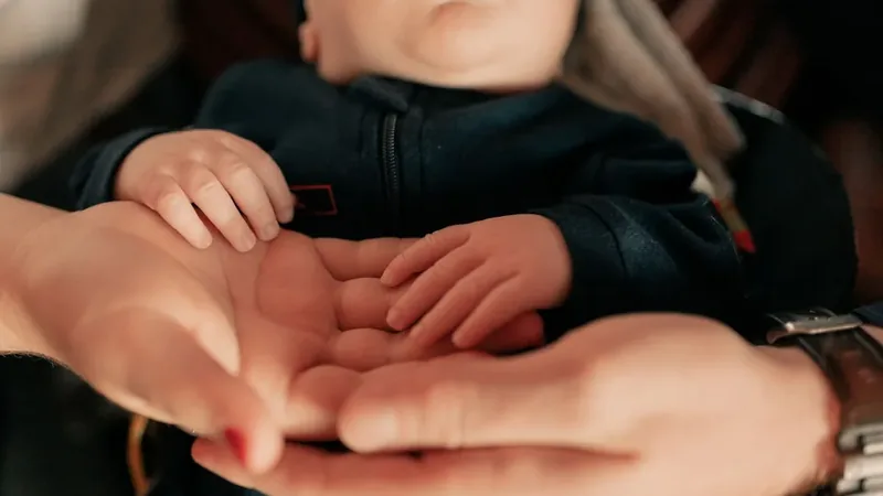Mãos de um bebê apoiadas nas mãos dos pais, idade em que o polegar em gatilho congênito é percebido