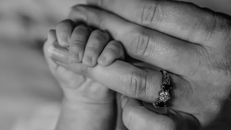 Mão de bebê segurando o dedo da mãe, fase em que a tenossinovite de De Quervain é comum